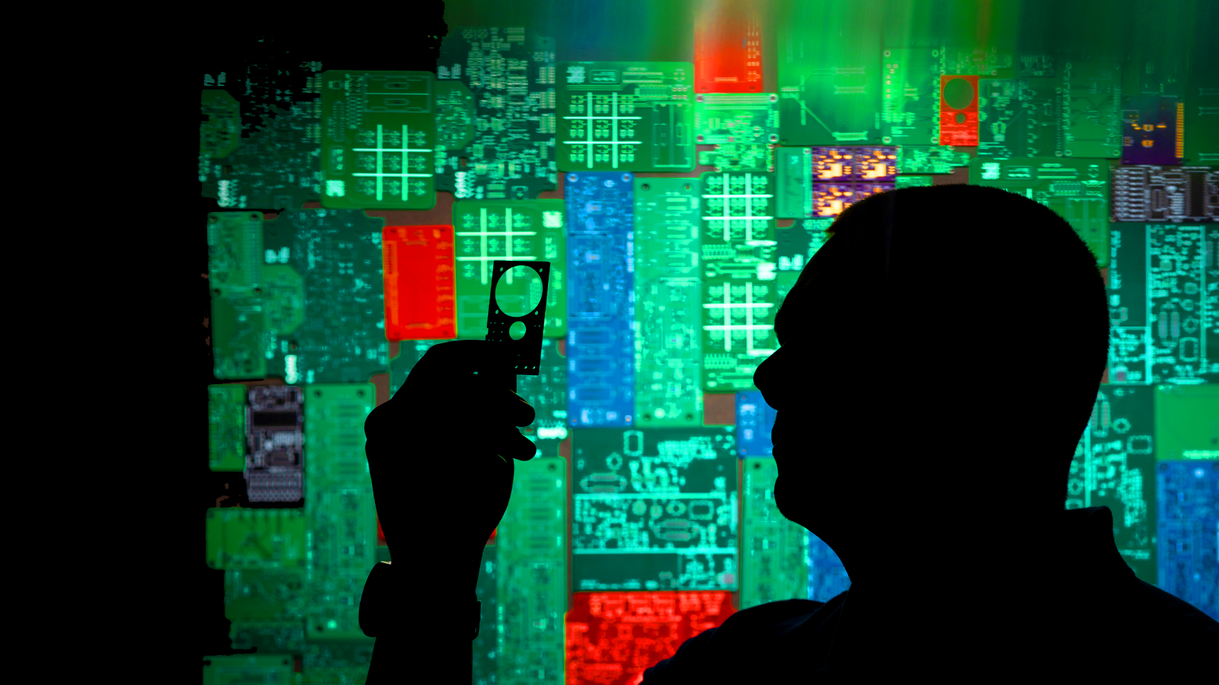 student holds a computer chip with a backdrop of circuit boards behind