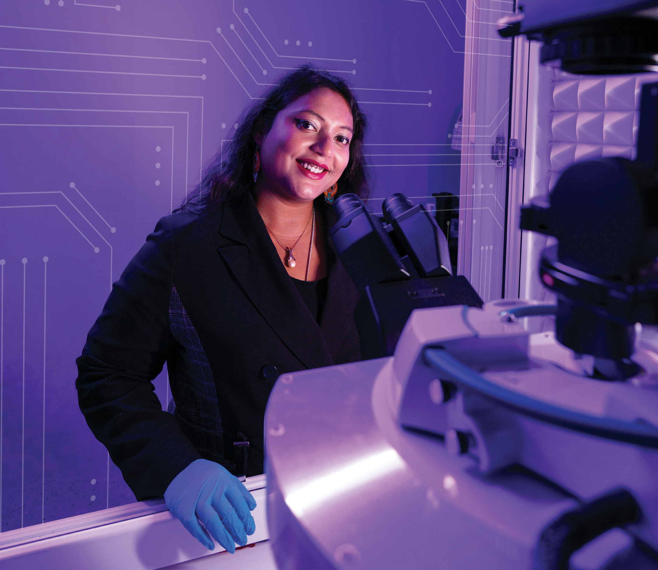 Anwesha Sarkar standing behind a microscope in lab setting